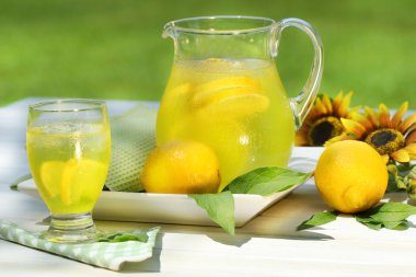 Pitcher of cool lemonade with glass on table clipart