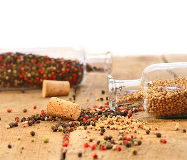 Peppercorns em garrafas de vidro na mesa de madeira — Fotografia de Stock