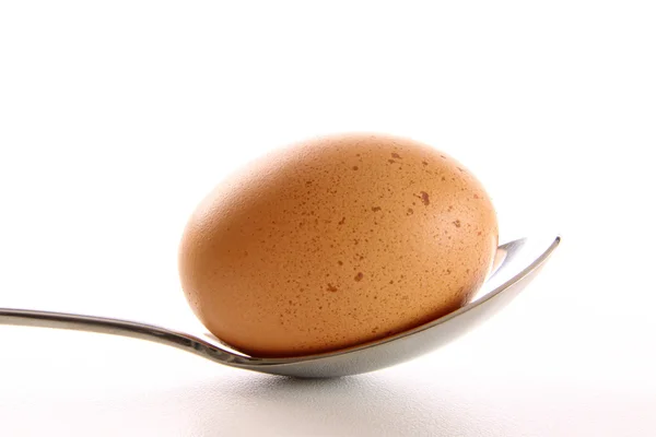 Uovo marrone con cucchiaio su bianco — Foto Stock