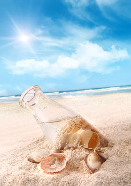 Бутылка с ракушками в песке — стоковое фото
