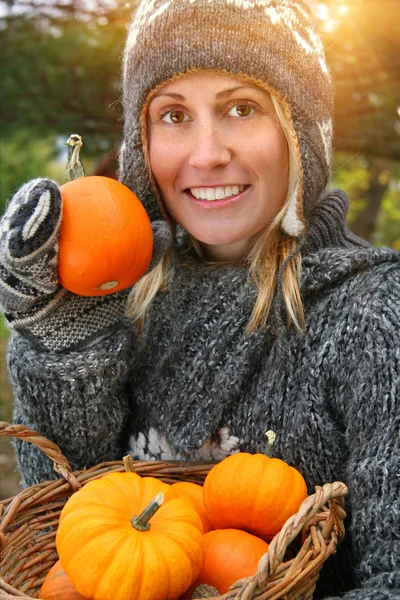 stock image Pretty young woman holding basket of pumpkins