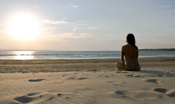 Młoda dziewczyna siedzi na bezludnej plaży — Zdjęcie stockowe