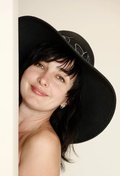 Όμορφη μελαχρινή γυναίκα με καπέλο, κοιτάζοντας πίσω από μια γωνία — Φωτογραφία Αρχείου