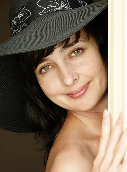 Όμορφη μελαχρινή γυναίκα στο καπέλο κοίταγμα πέρα δώθε πίσω από μια κουρτίνα — Φωτογραφία Αρχείου