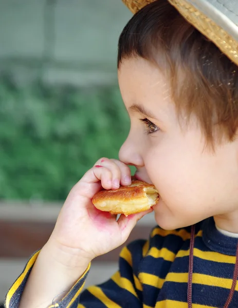 Little boy in straw hat eats doughnut — Stock Photo, Image