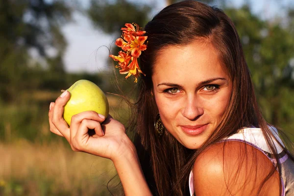 Woman holding apple with flower in hair — Stock Photo, Image