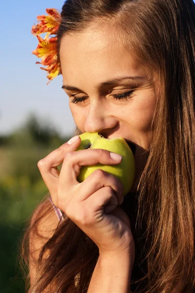 Молодая девушка кусает яблоко, цветы в волосах — стоковое фото