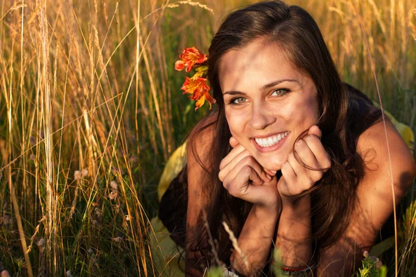 Krásná dívka s květinou ve vlasech na trávě, opřel se rukou — Stock fotografie