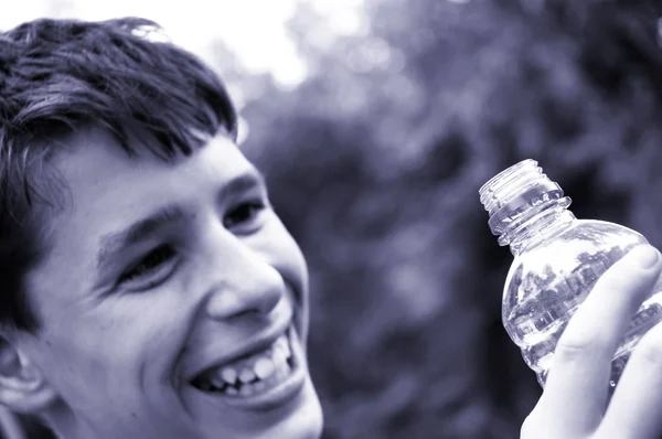 Sorriso suave do menino e garrafa azul — Fotografia de Stock