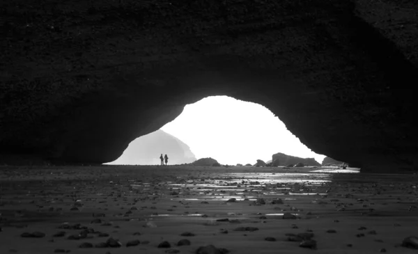 Jong koppel, wandelen onder boog rotsformatie in de buurt van de Atlantische Oceaan in Marokko — Stockfoto