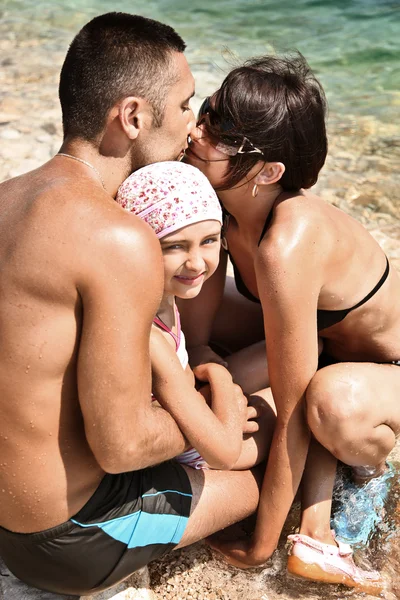 Mladá rodina zahrnující na písečné pláži — Stock fotografie