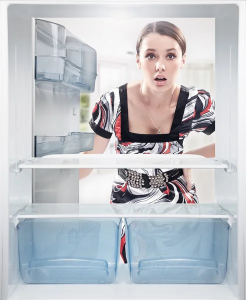 Junge Frau blickt auf leeres Regal im Kühlschrank. — Stockfoto