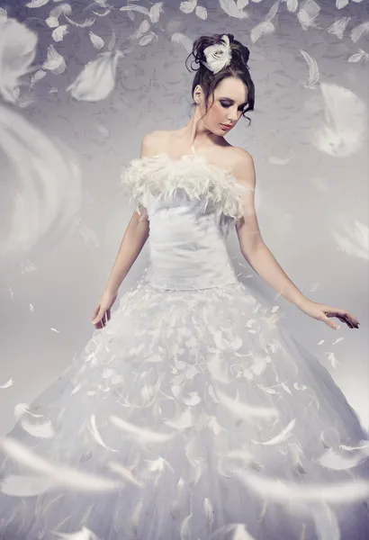 Hermosa novia posando sobre plumas voladoras blancas Imagen de archivo