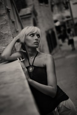 Portrait of young woman smoking cigarette in old city street background. clipart