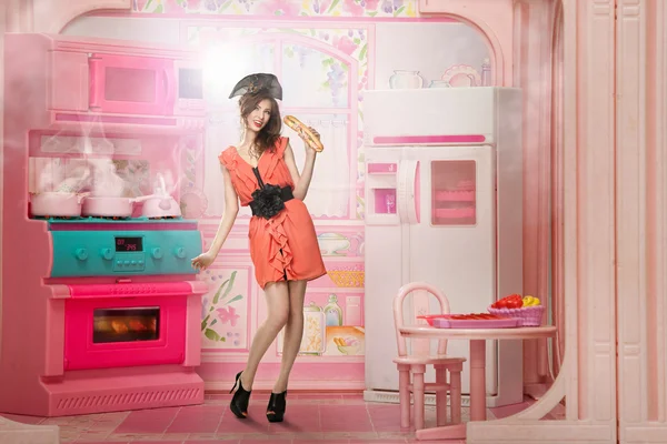 Jovem mulher como uma boneca cokking na cozinha rosa — Fotografia de Stock