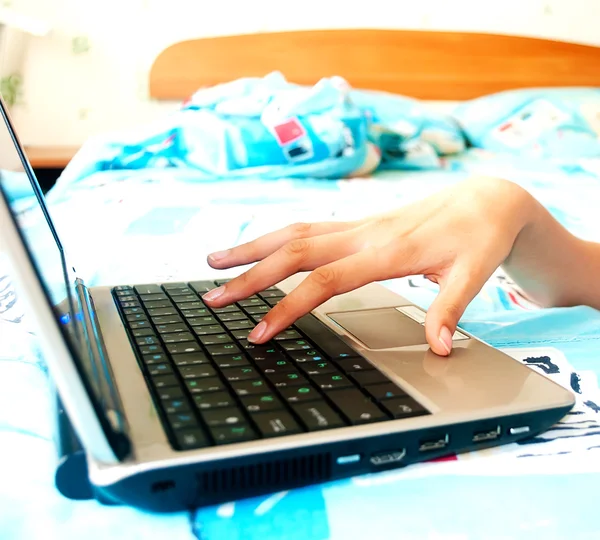Frauenhände tippen auf einem silbernen Laptop auf dem Bett. — Stockfoto