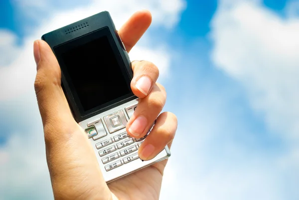Mobilní telefon v ruce na pozadí modré oblohy. — Stock fotografie