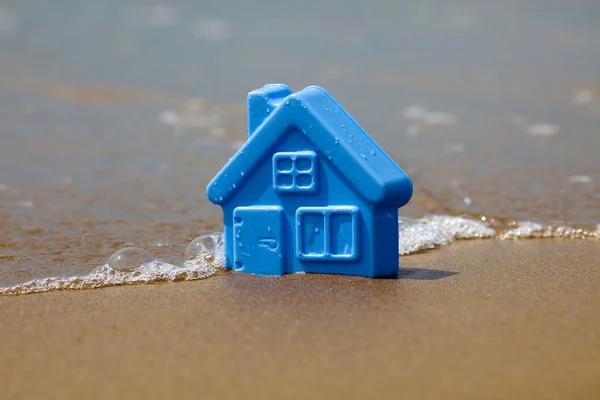 Toy plastic house on the sand washes wave — Stockfoto