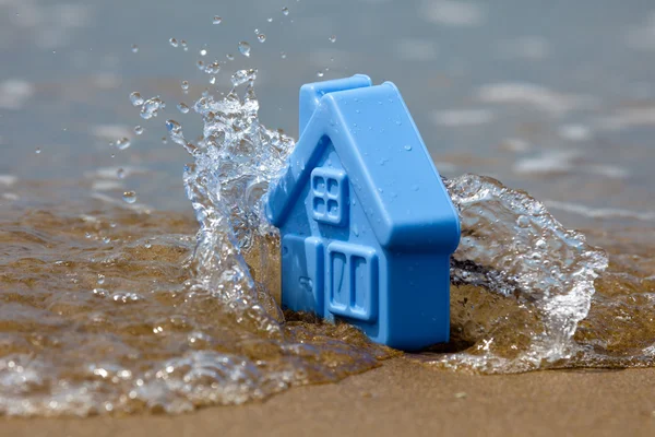 Игрушечный пластиковый дом на песке смывает волну — стоковое фото