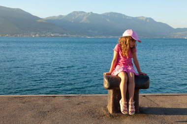 The little girl in a pink dress sitting on a bollard in the mari clipart