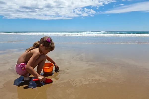 Dívka hraje s rýč a džber na mokrém písku — Stock fotografie