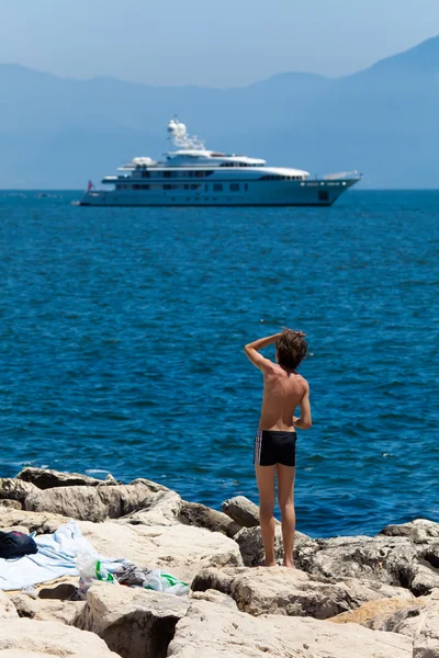 A boy on a brick bank admires luxury white yacht — Stock Photo, Image