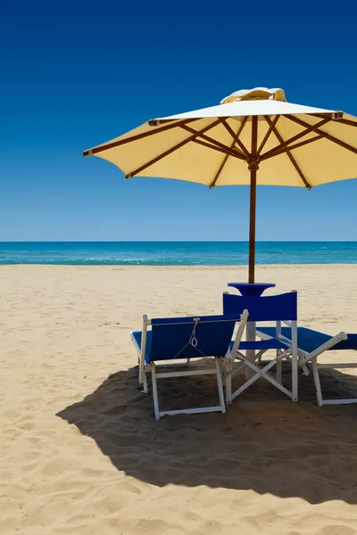 Liegestühle unter einem Sonnenschirm im Sand — Stockfoto