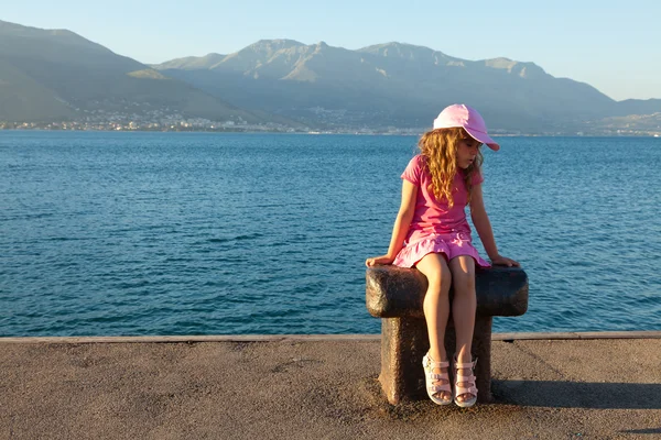 stock image The little girl in a pink dress sitting on a bollard in the mari