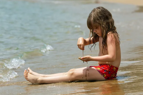 Küçük kız dalgalar bir plajda otururken — Stok fotoğraf