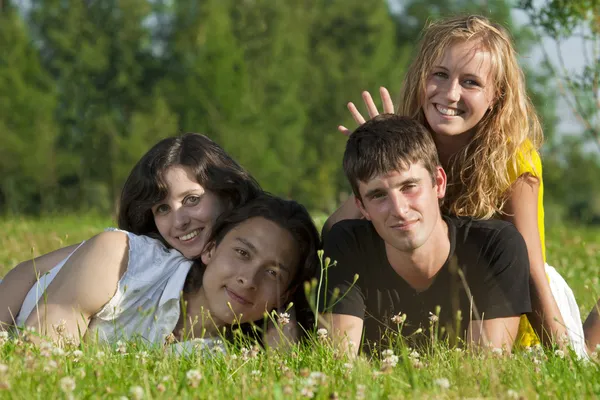 Cuatro hombres jóvenes - dos niñas y dos hombres acostados en la hierba en th —  Fotos de Stock