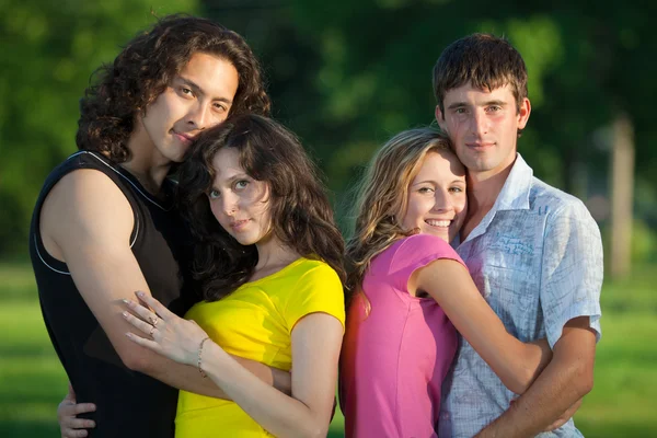 Vier junge Menschen umarmen und stehen im Park — Stockfoto