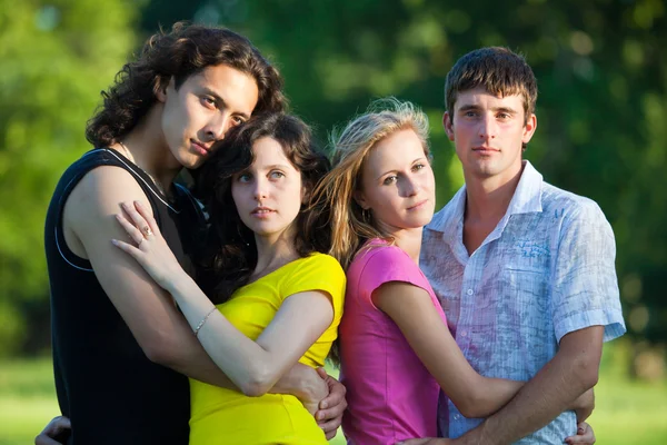 Vier junge Menschen umarmen und stehen im Park — Stockfoto