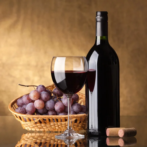 En flaska rött vin, glas och druvor Stockbild