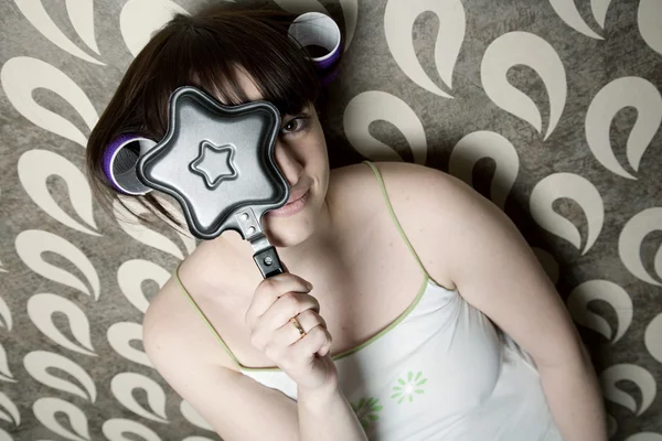Young adult girl with frying pan star and hair rollers have fun — Stock Photo, Image