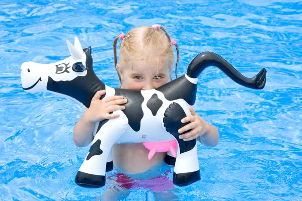快乐的小女孩在一个游泳池与玩具牛 — 图库照片