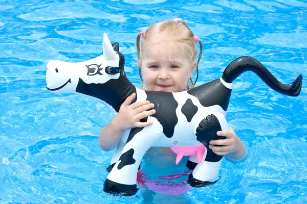 快乐的小女孩在一个游泳池与玩具牛 — 图库照片