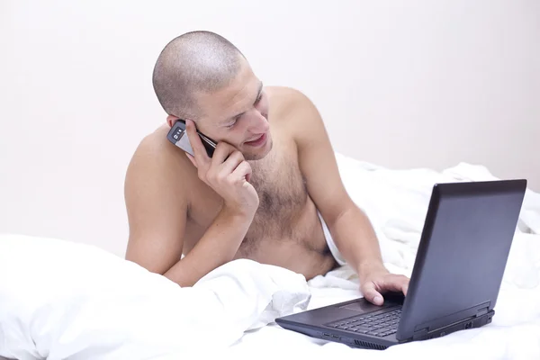 Homem inteligente falando no celular com um laptop na frente — Fotografia de Stock