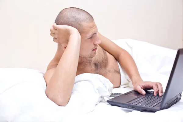 Mężczyznę leżącego w łóżku, patrząc na jego laptopie — Zdjęcie stockowe
