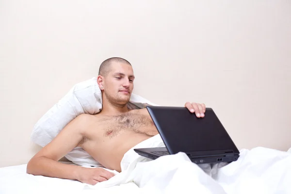 Muž leží v posteli, při pohledu na jeho laptopu — Stock fotografie