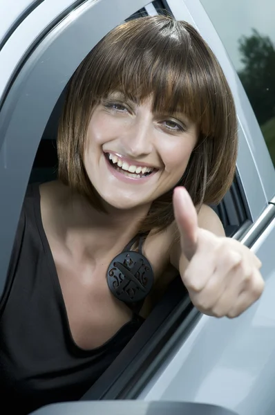 Happy woman in a car with thumbs up. — Stock Photo, Image