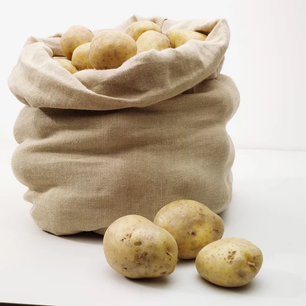 Overflowing bag of potatoes on whit — Stock Photo, Image