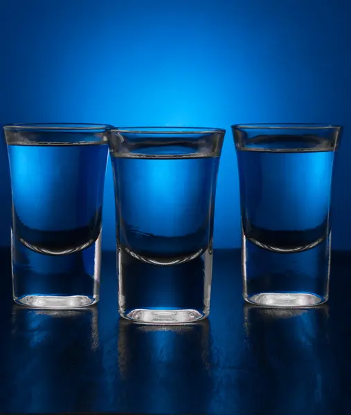 Три стакана водки на голубом фоне — стоковое фото