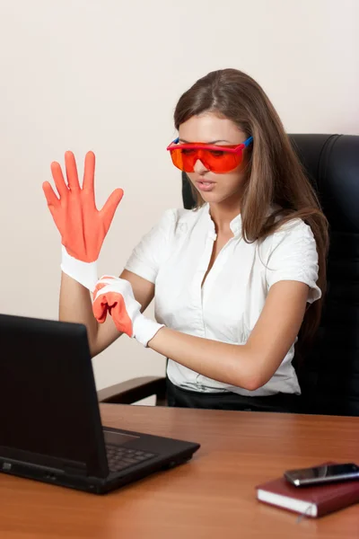 Молодая женщина за столом с ноутбуком в перчатках и оранжевом Стоковое Фото