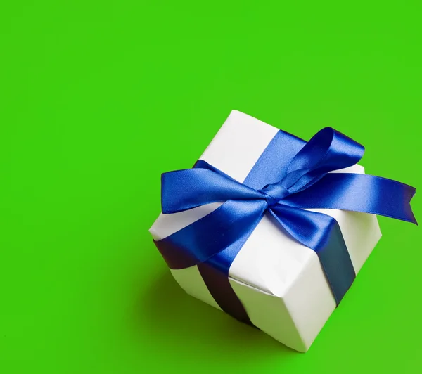 Biały prezent w niebieską wstążką na zielonym tle — Zdjęcie stockowe