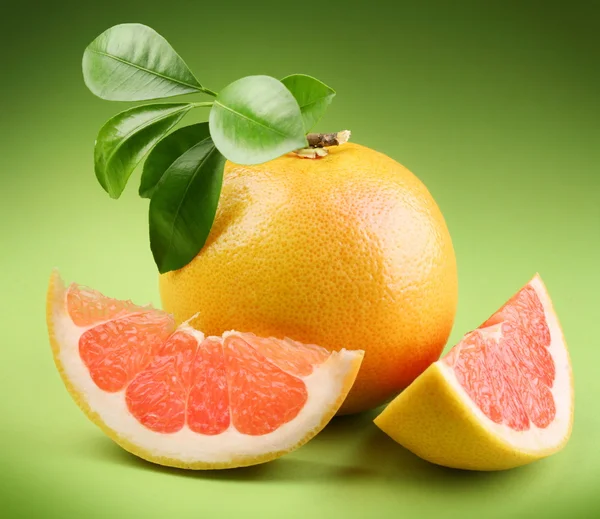 Reife Grapefruit mit Segment auf grünem Hintergrund — Stockfoto