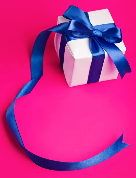Biały prezent w niebieską wstążką na różowym tle — Zdjęcie stockowe