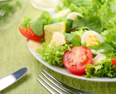 Fresh salad with tomato and quail eggs in a white bowl on a green tableclot clipart