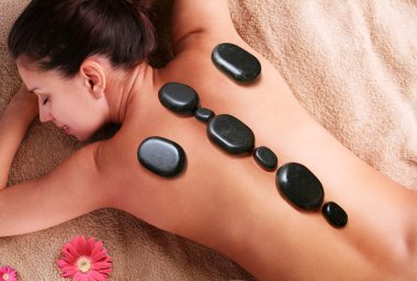 Smiling young woman getting pleasure of stone therapy. Eyes are closed. clipart