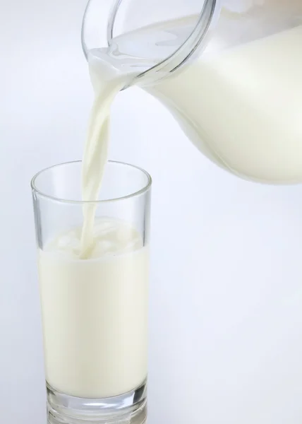 Pouring of milk from jar into a glass — Stock Photo, Image