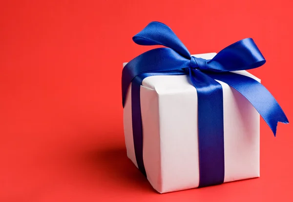 White gift with a blue ribbon on a red background — Stock Photo, Image